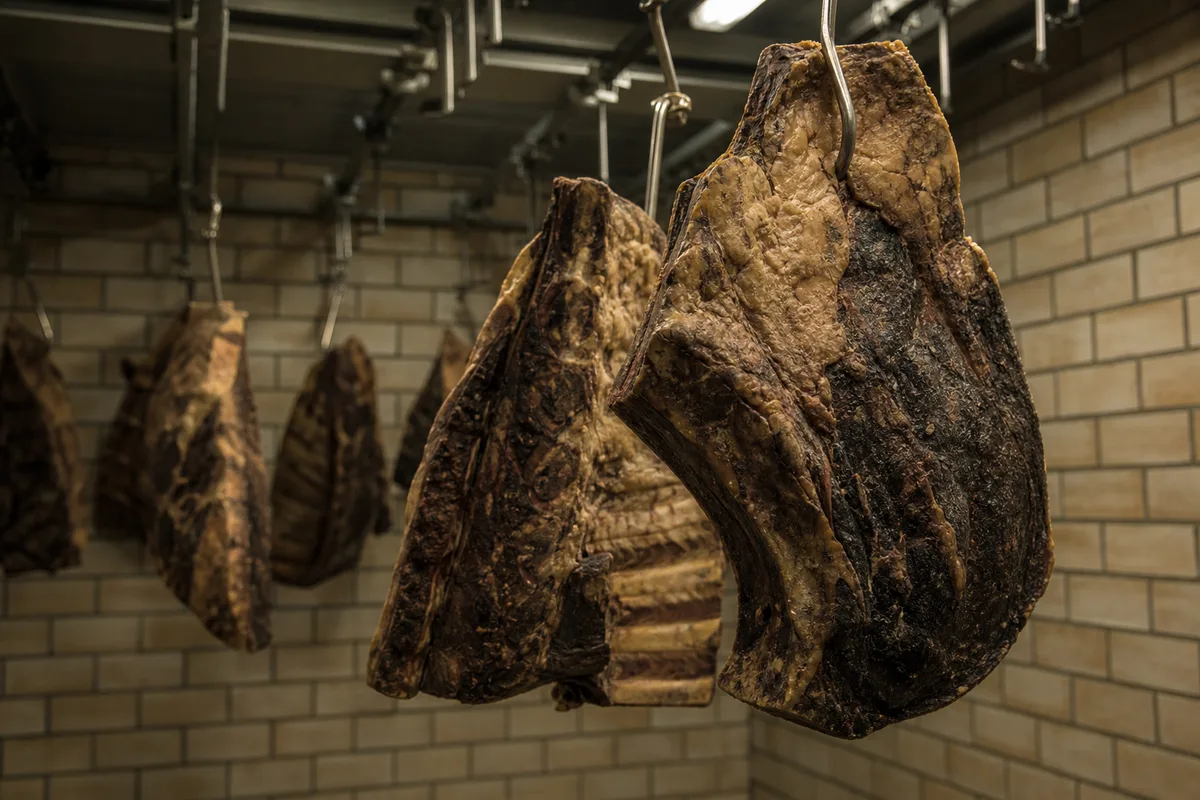 Pièces de boeuf suspendues dans une chambre de maturation de boucherie artisanale, lumière tamisée, croûte sèche sur la surface