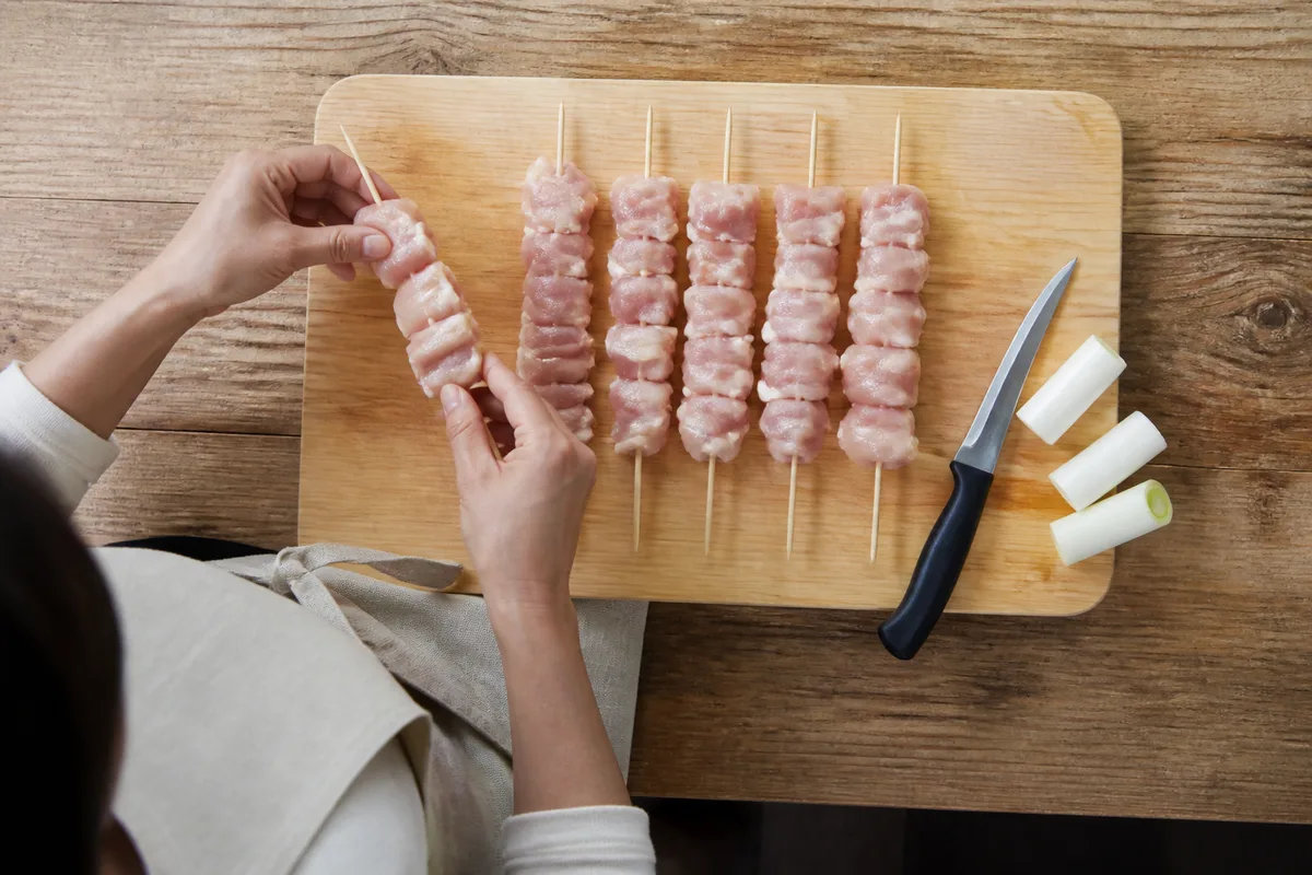 Dés de haut de cuisse de poulet enfilés sur des piques de bambou, posés sur une planche de bois clair